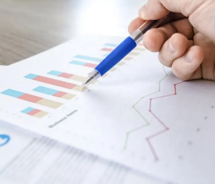 A pen pointing at bar and line charts on a printed financial report
